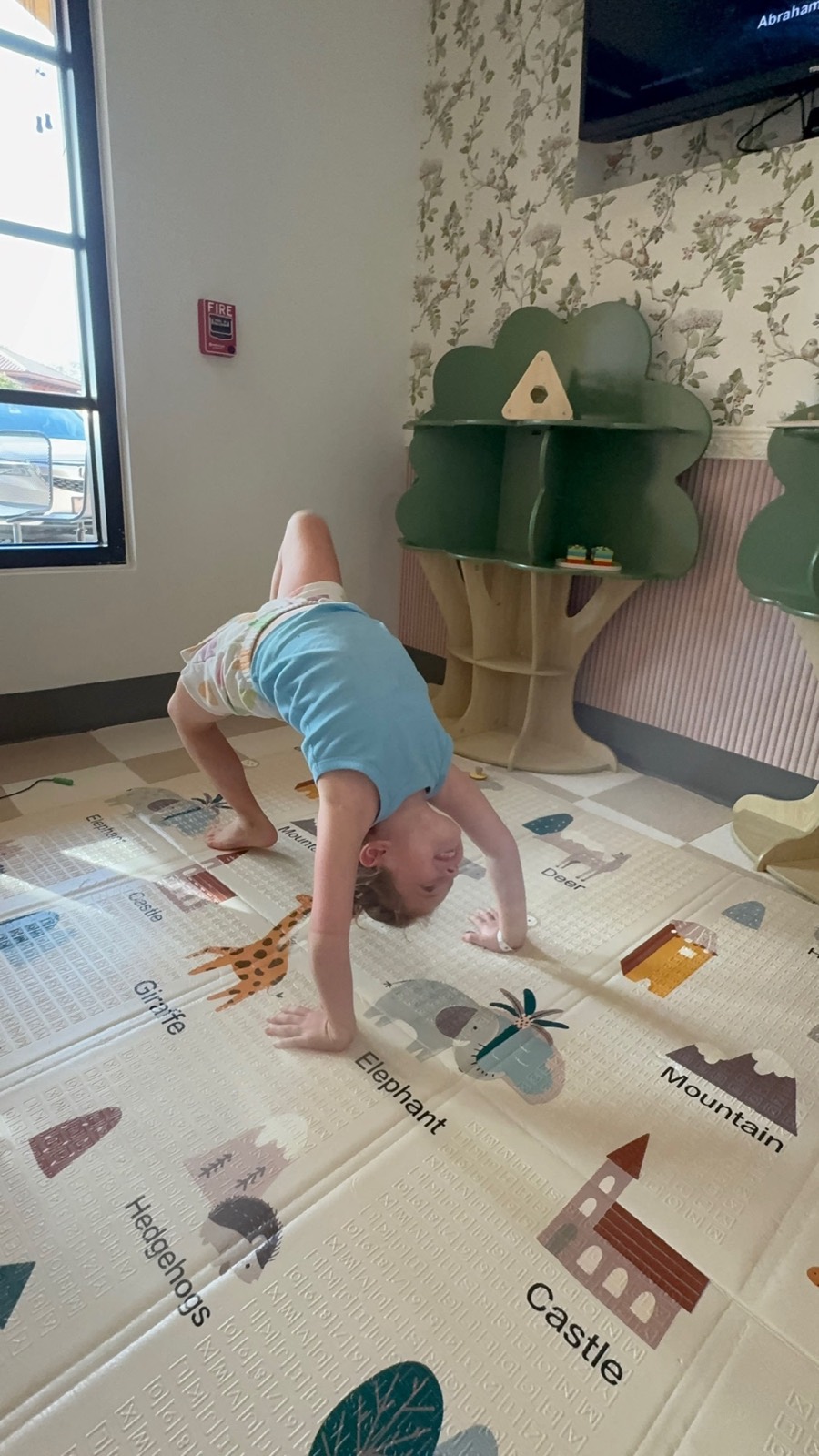 A toddler plays on the mat beside the treehouse shelves.
