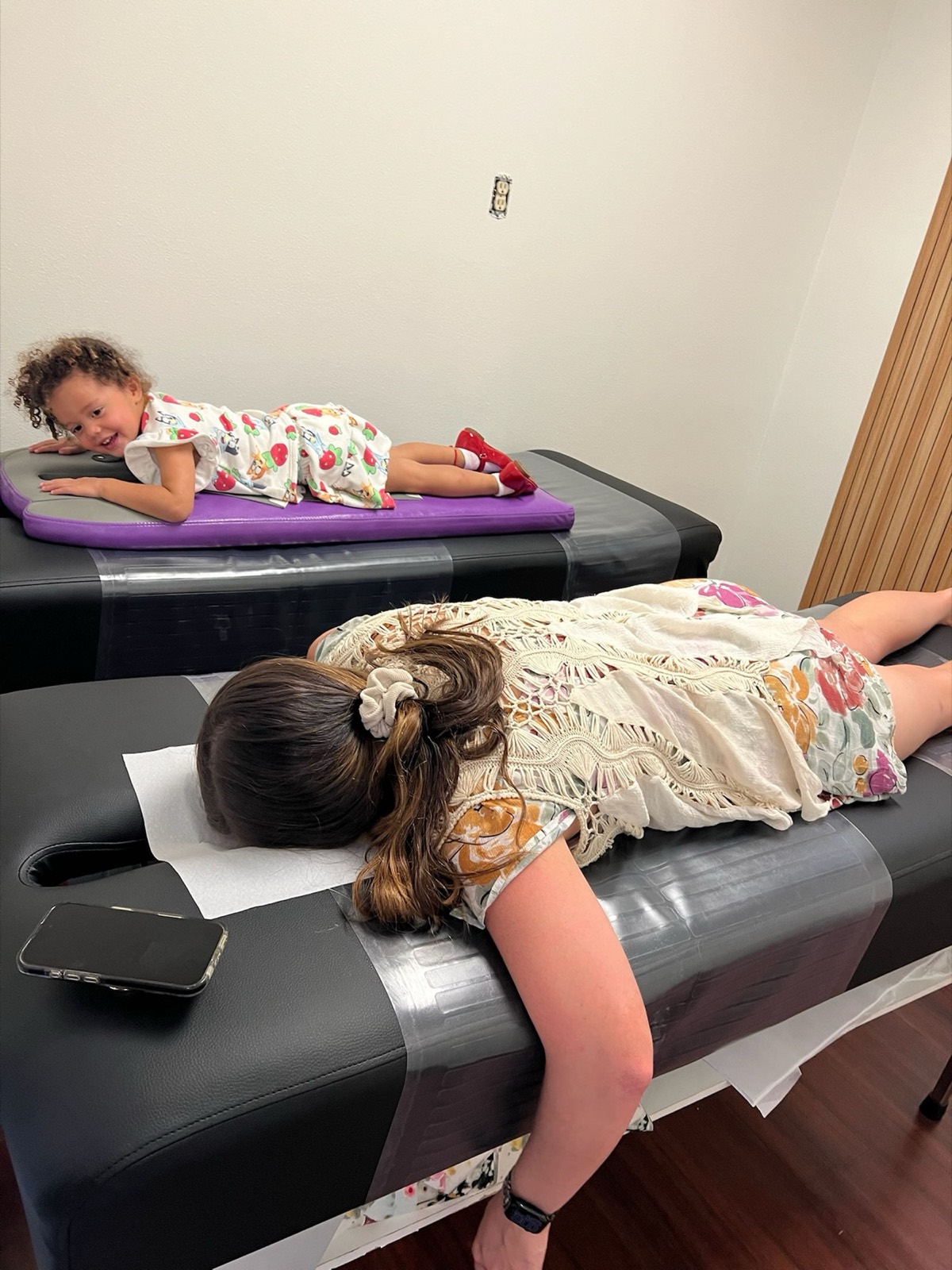 A toddler lies on the pediatric table while mom is checked on the next table.