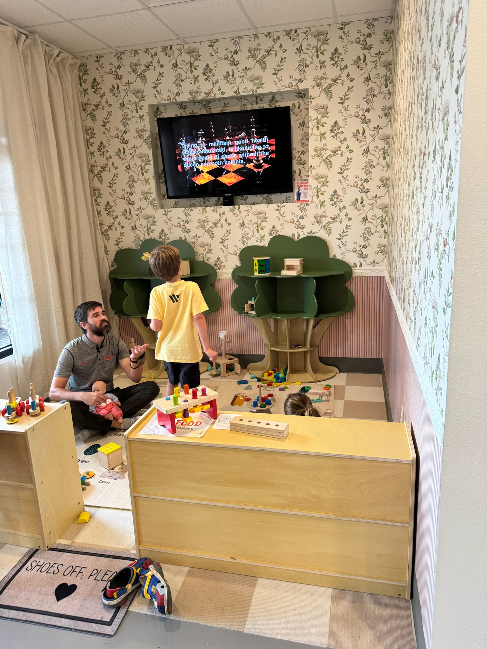 Dr. Fox plays on the floor with children in the Little Roots treehouse area.