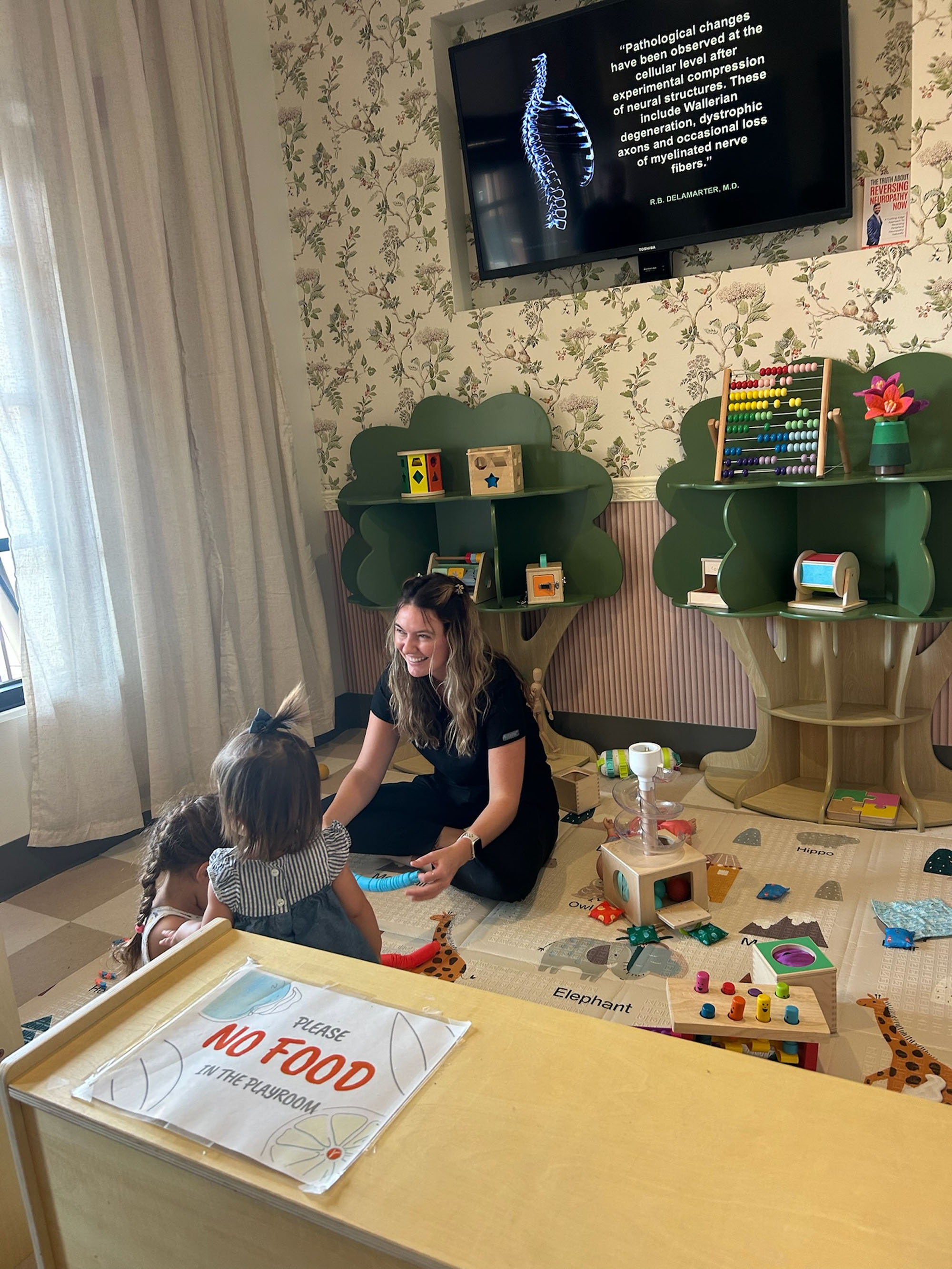 Carly Lovato with two young children by the Little Roots tree shelves.