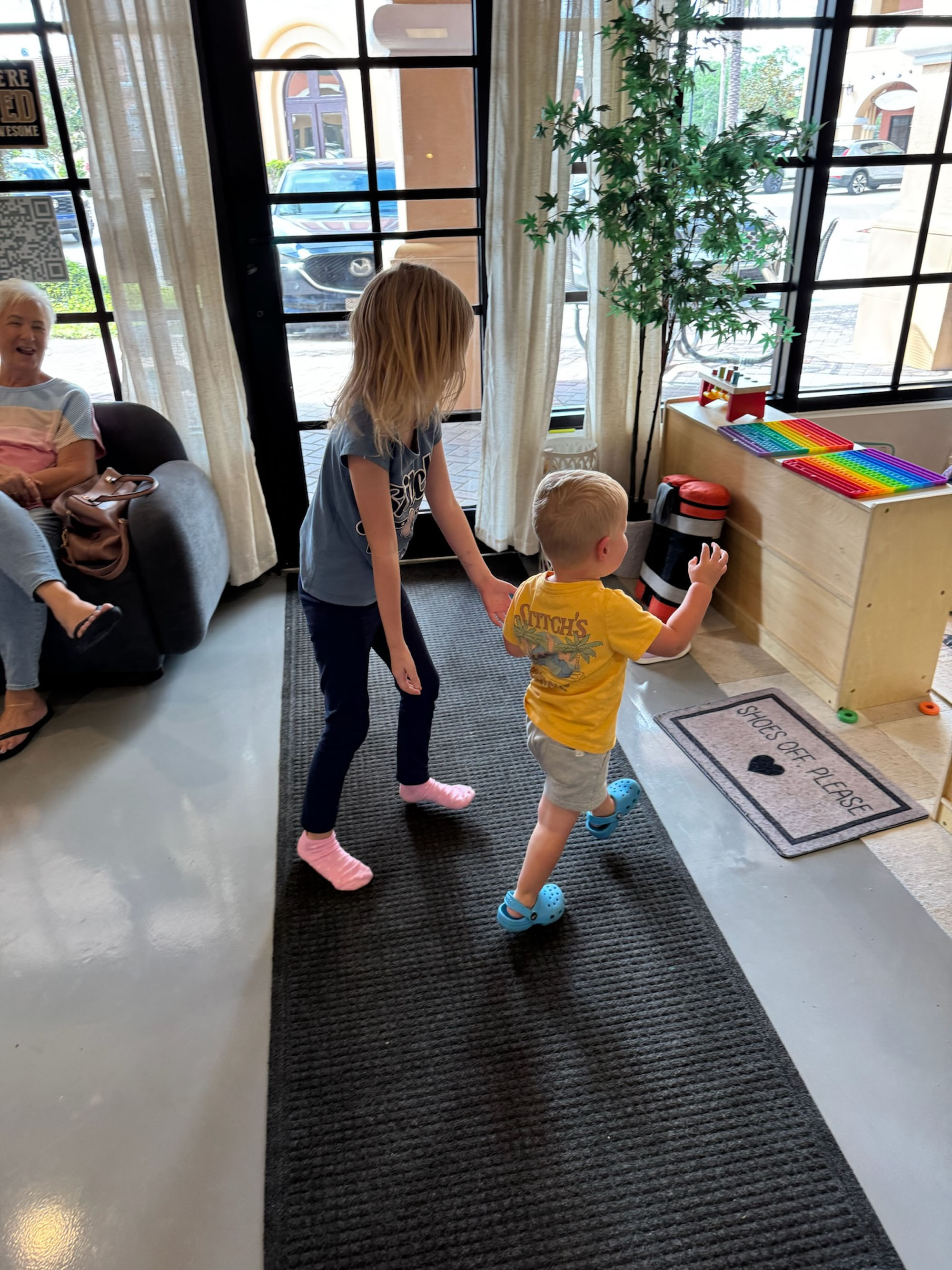 A young girl and toddler boy dance together in the Little Roots lobby.