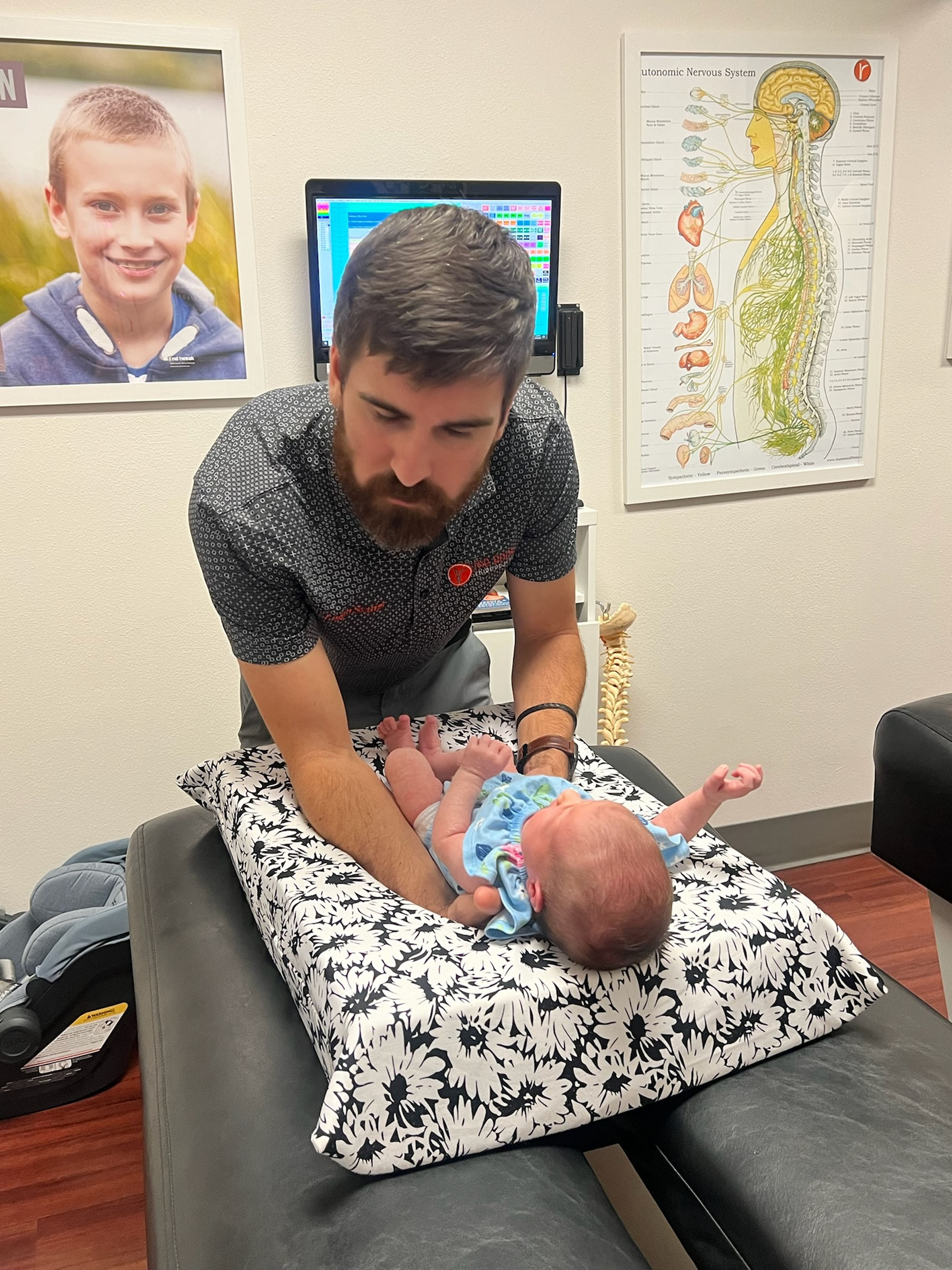 A Roots doctor adjusts a newborn in front of the autonomic nervous system chart.