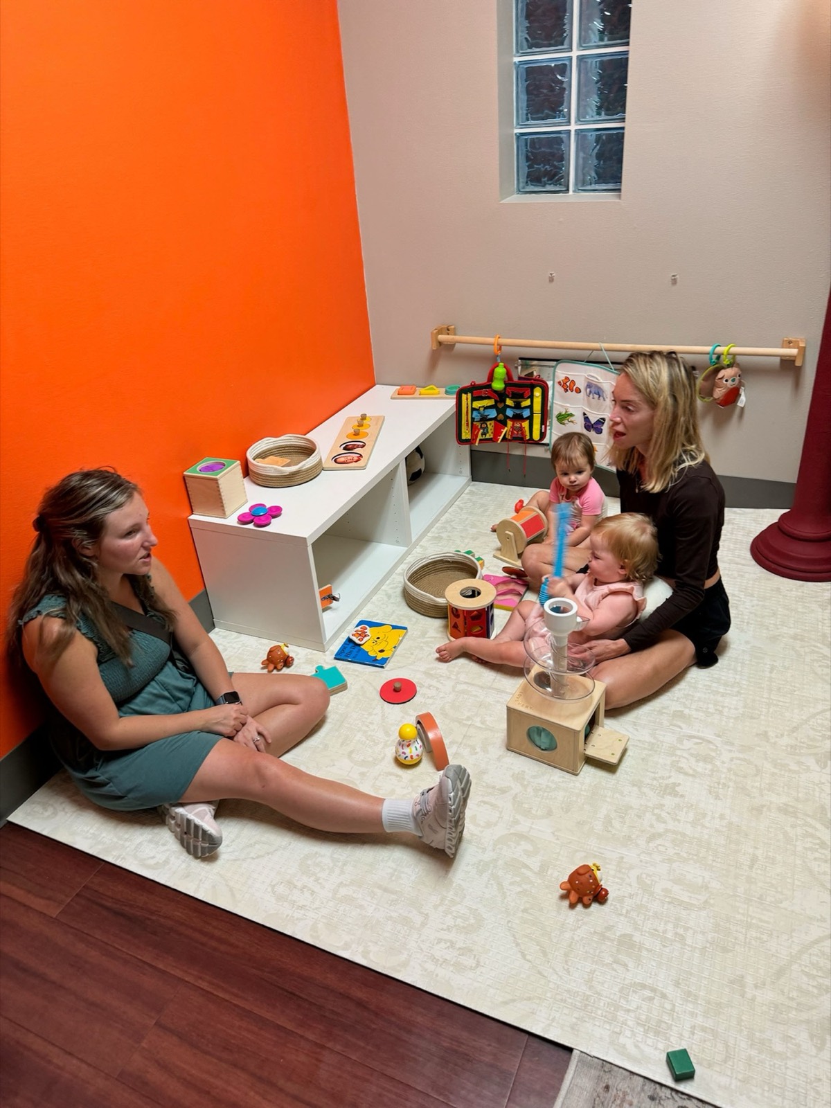 Two moms talk in the Little Roots play corner while their little ones play.