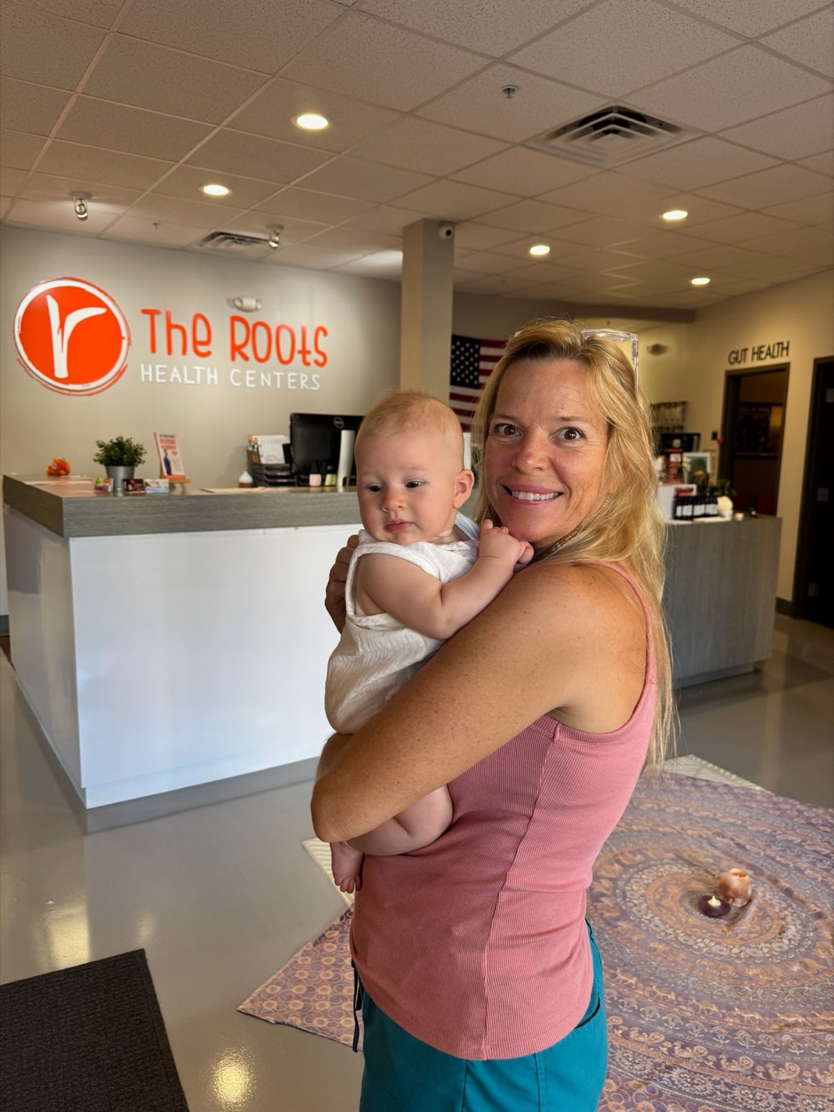 A mother holds her infant in front of The Roots logo wall at reception.