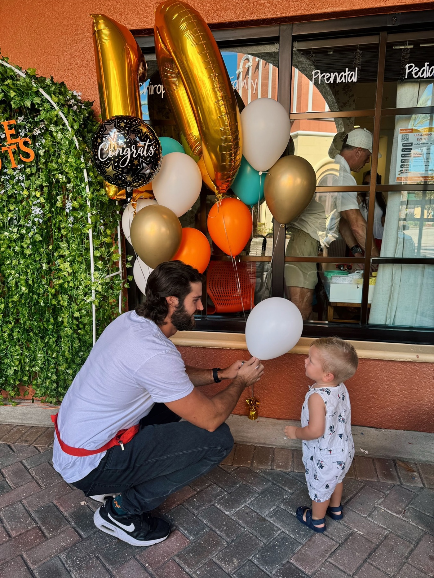 Dr. Fox kneels to hand a balloon to a young child at a clinic event.