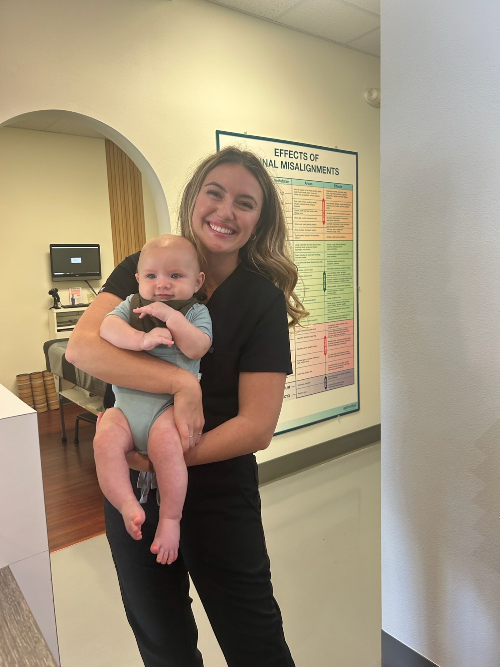 Carly holds a happy baby near the spinal effects chart.